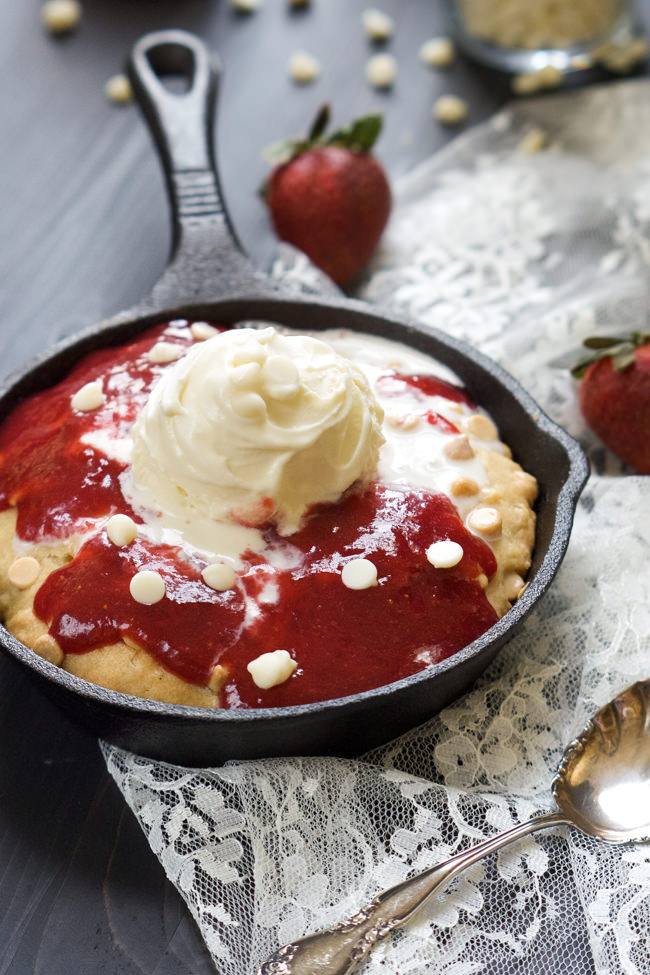 A decadent White Chocolate Sugar Cookie Skillet that is simple to make, topped with vanilla custard and drizzled with a gooey homemade strawberry sauce! #skillet #cookie #whitechocolate #icecream
