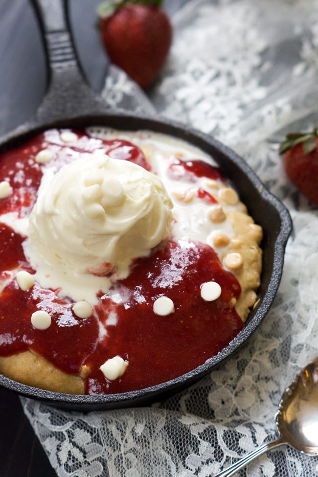 A decadent White Chocolate Sugar Cookie Skillet that is simple to make, topped with vanilla custard and drizzled with a gooey homemade strawberry sauce! #skillet #cookie #whitechocolate #icecream
