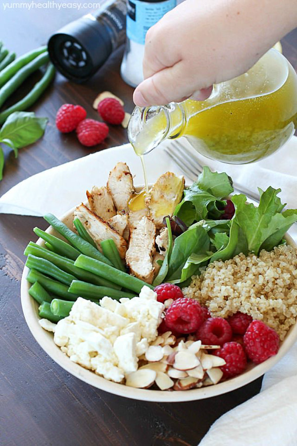 A yummy salad bowl that is full of grilled chicken, cooked quinoa, kale salad mix, fresh raspberries, sliced almonds, feta cheese, green beans and a homemade basil vinaigrette.