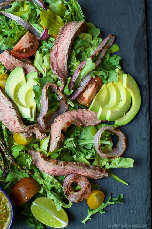 A paleo California Steak Salad filled with grilled onions, arugula, avocado, asparagus, charred Steak and covered in zesty Chimichurri Dressing. Fresh, light, high in protein and freakin delicious! You need this!